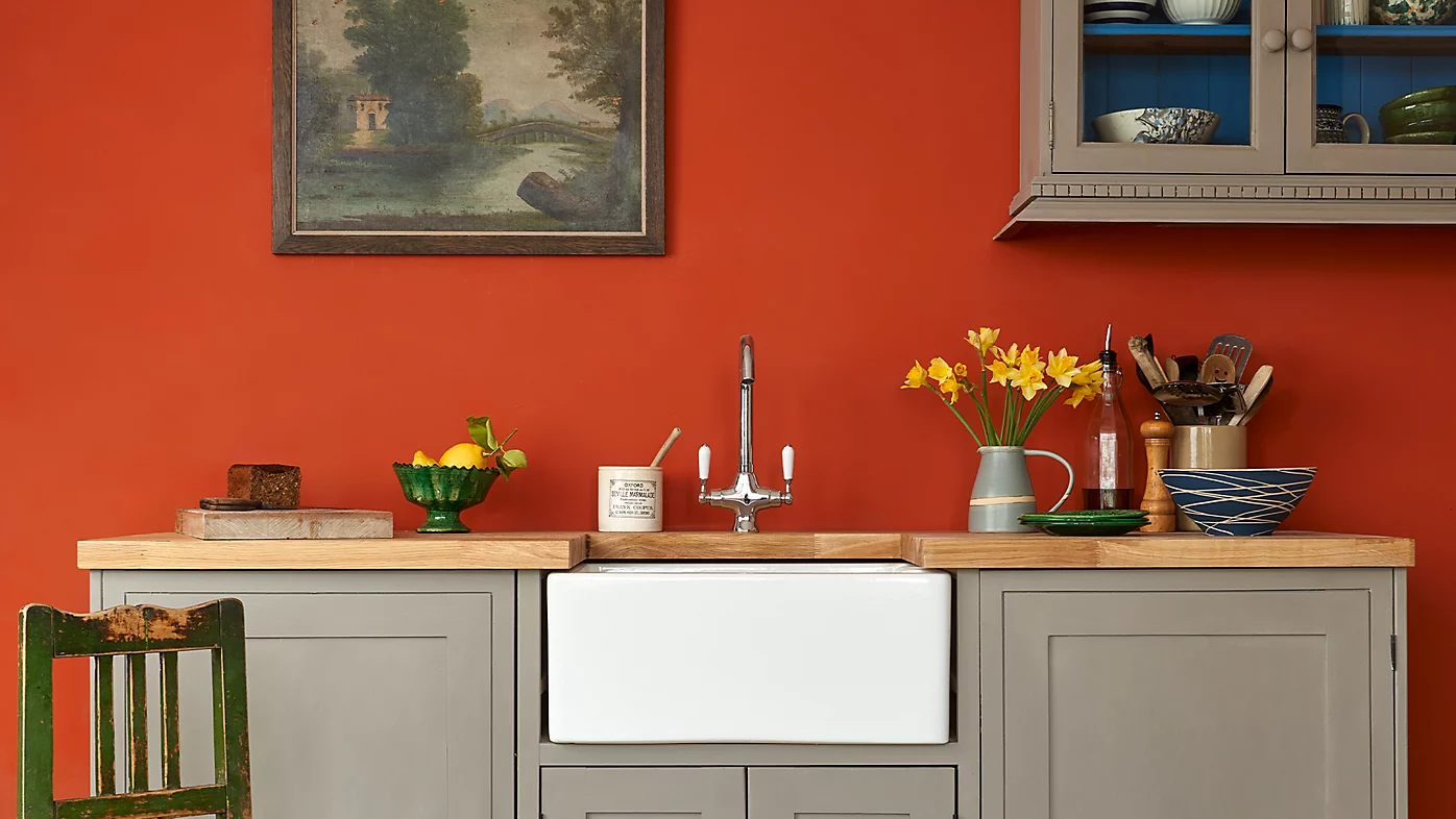 Kitchen with gray cabinets, wooden countertop, and green chair against a red wall.